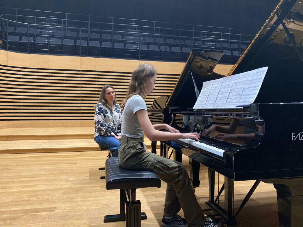 a woman sitting at a piano with a girl playing the piano