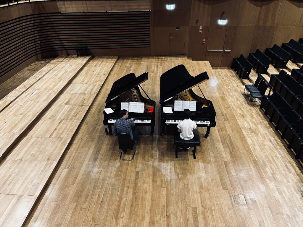 Dwóch pianistów gra na fortepianach.